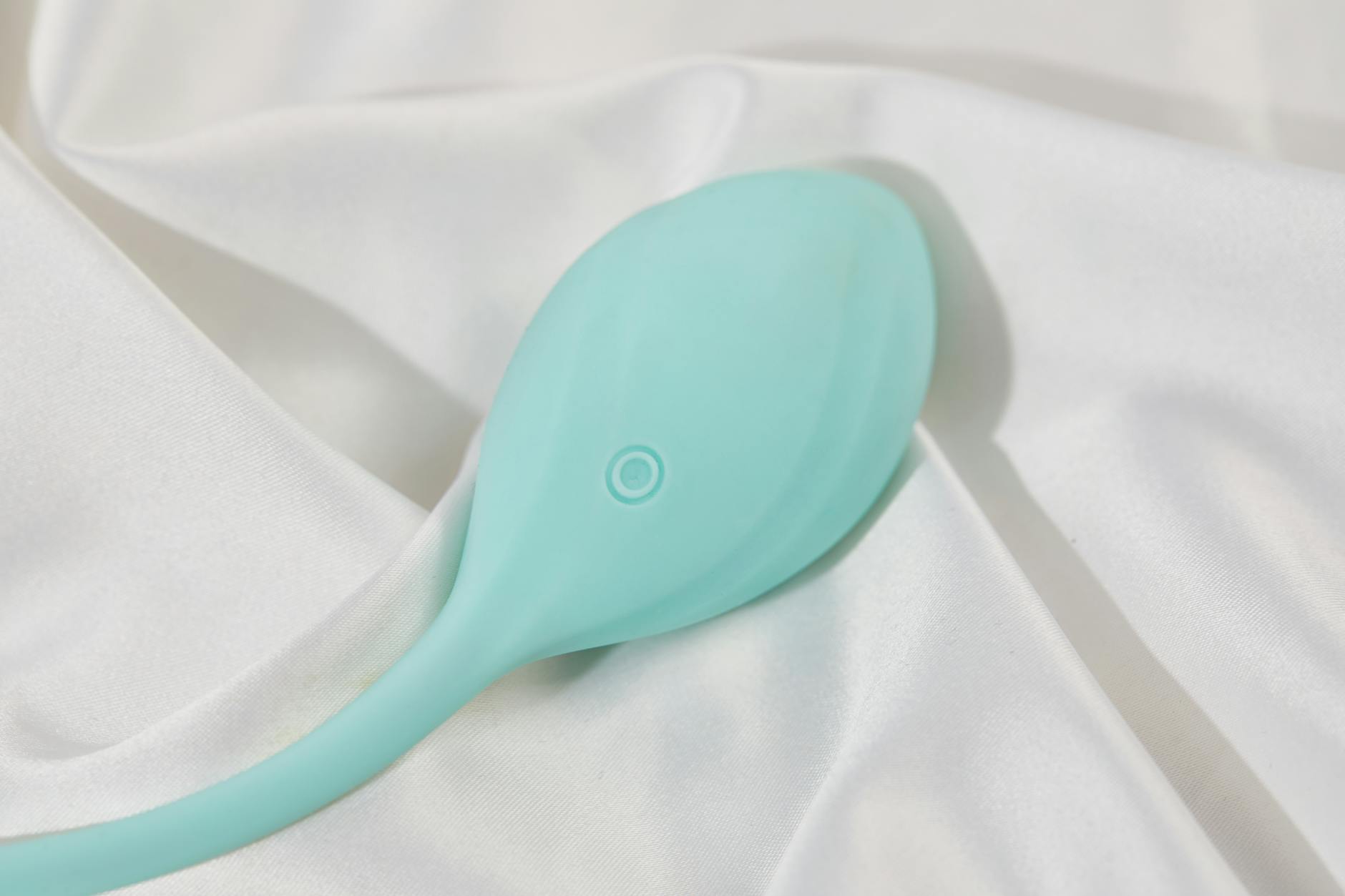 A teal clitoral vibrator resting on smooth white silk, symbolizing pressure-free pleasure