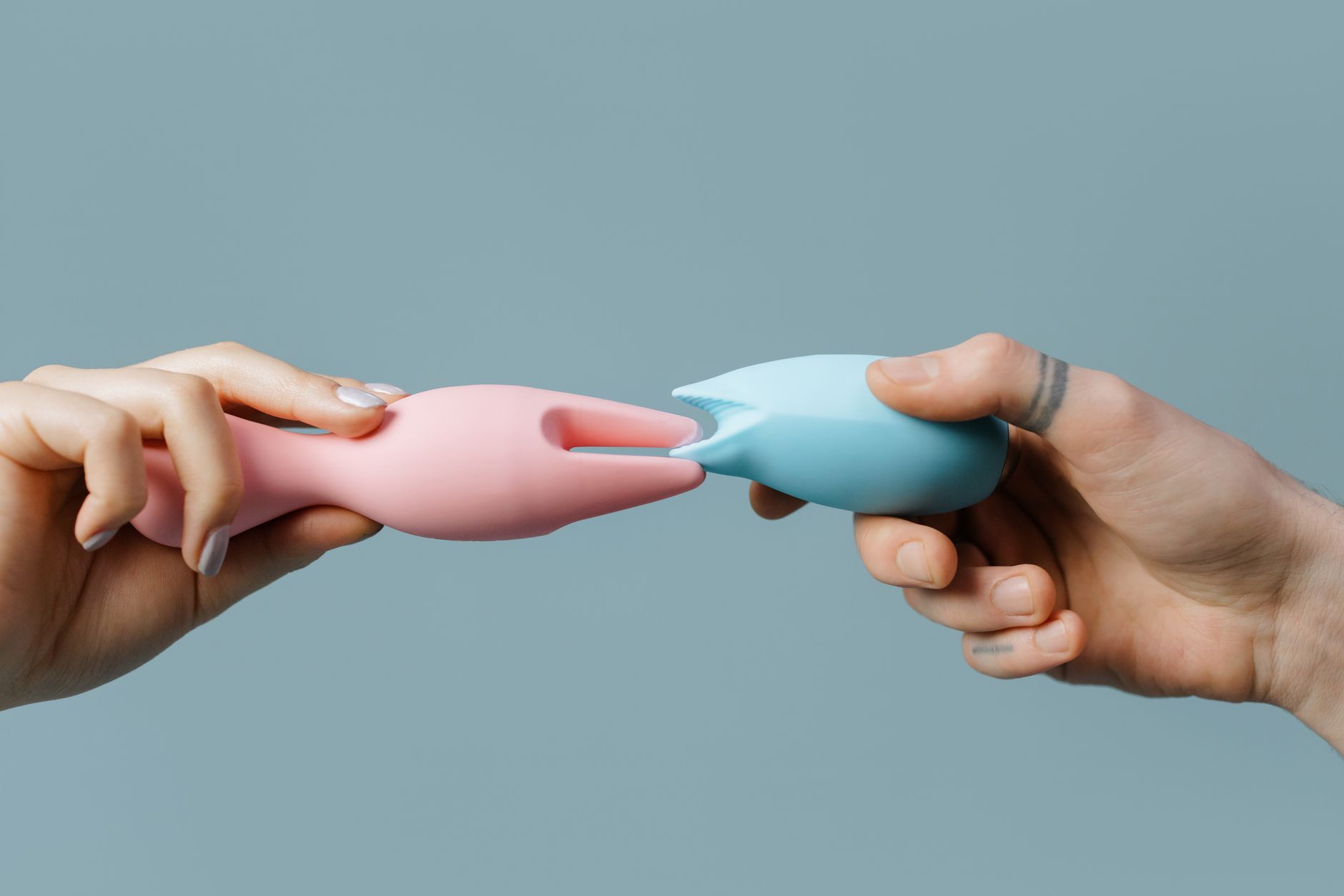 Two hands holding vibrators in pink and blue against a soft pastel background