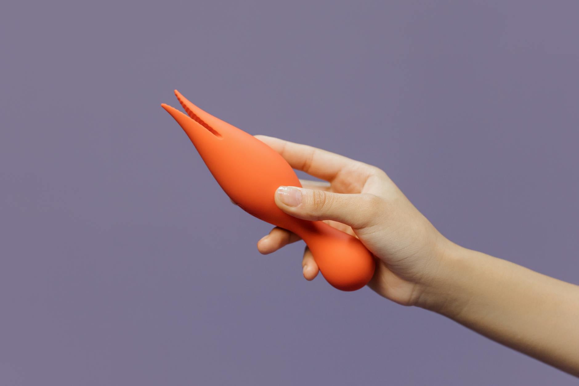 Close-up of a hand holding a vibrator against a minimalistic purple backdrop, showcasing modern sensuality