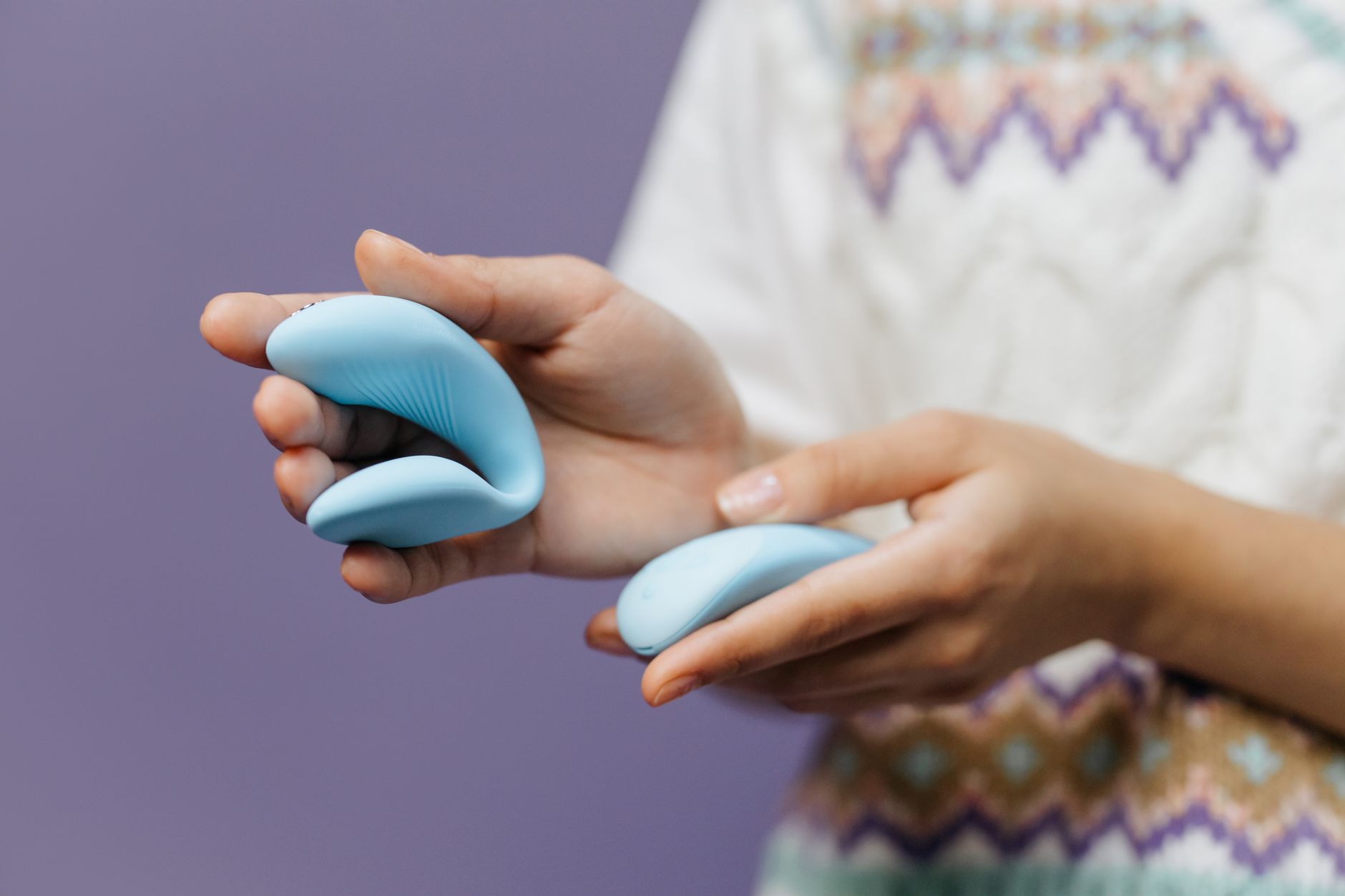 Hands holding a sleek blue vibrator against a purple background, symbolizing intimate connection and body reconnection