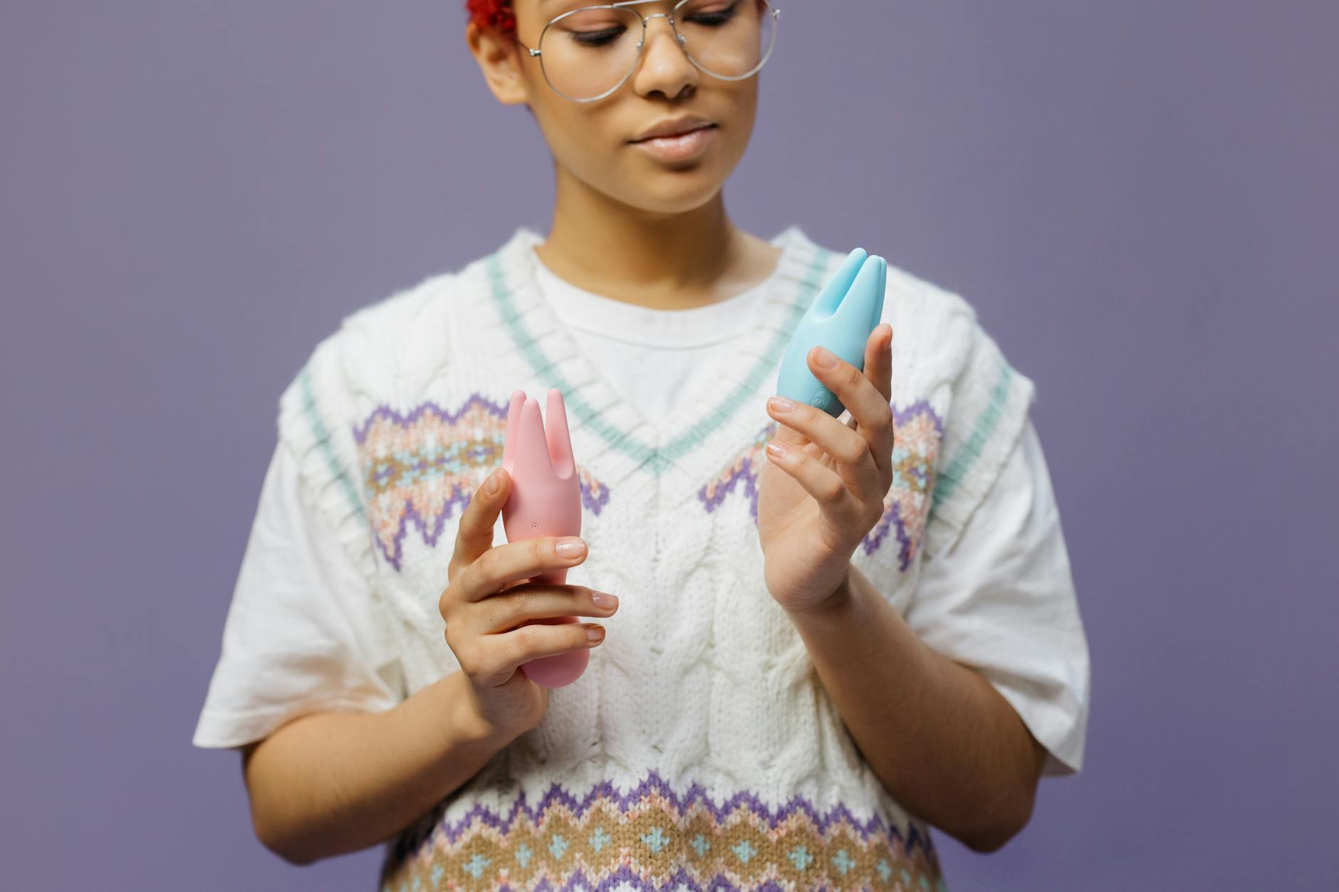 A young woman holding two colorful vibrators, representing solo pleasure during long-distance separation.