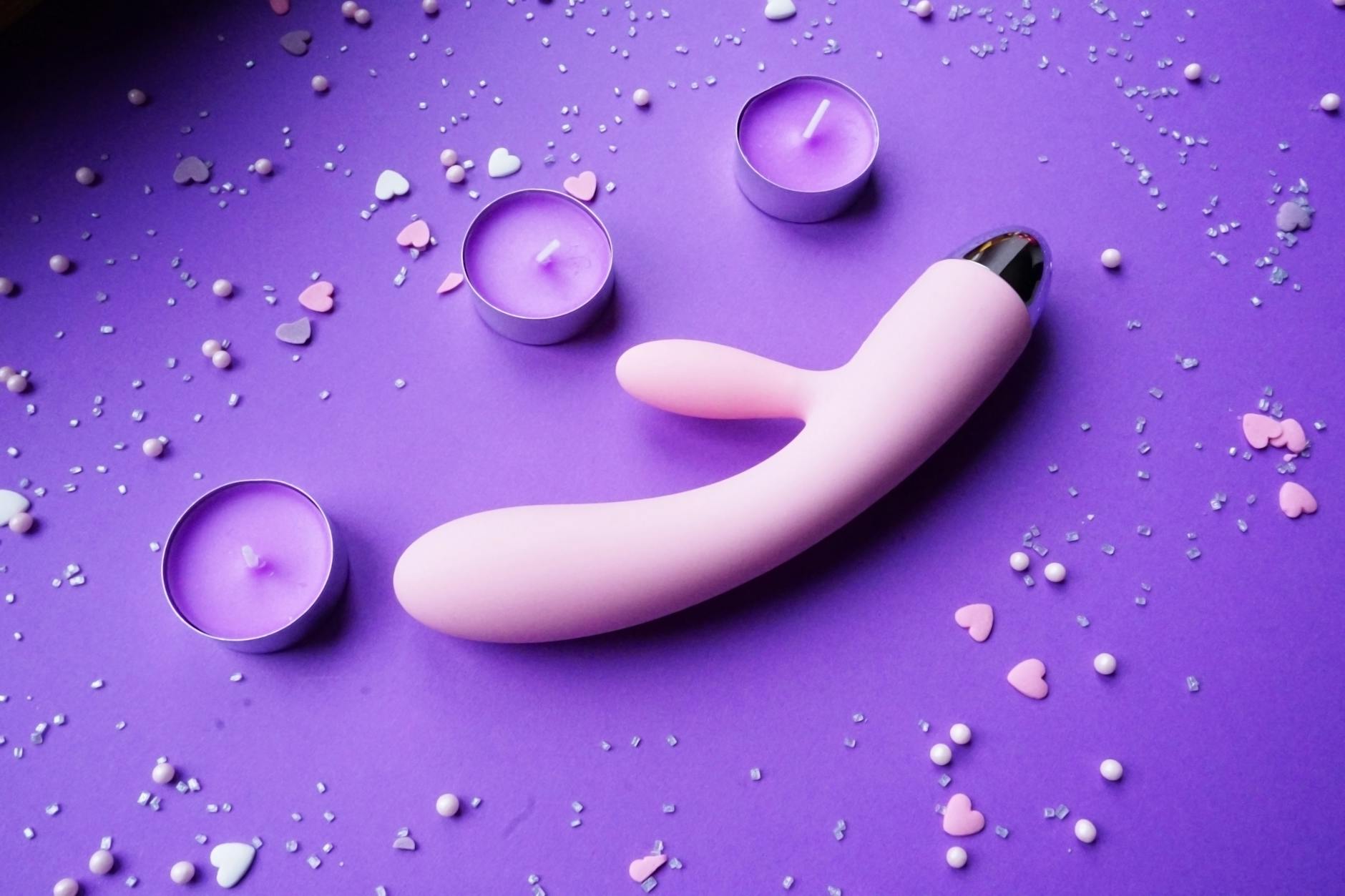 A lemon clitoral vibrator on a purple background with pink confetti and candles